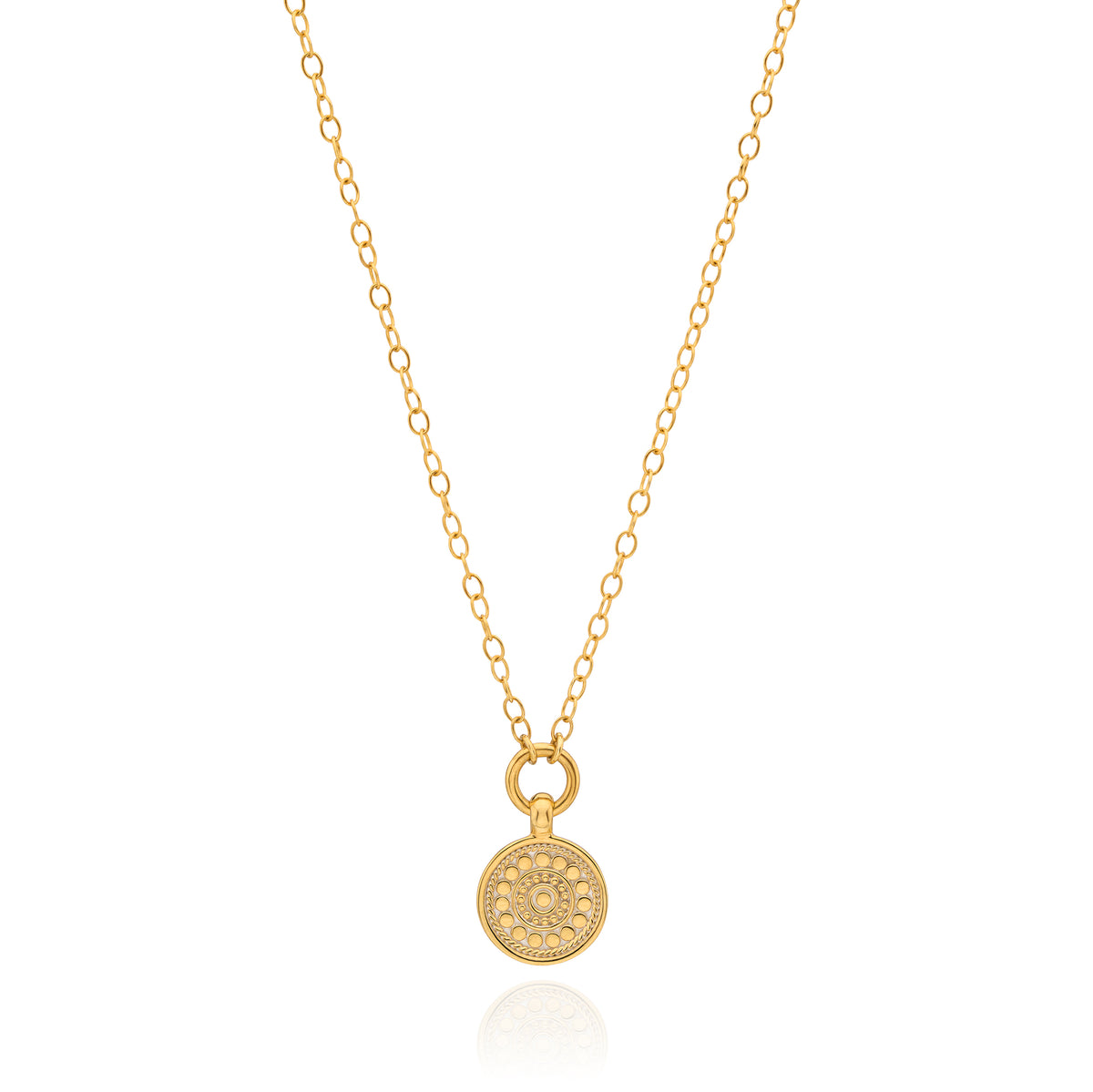A delicate gold chain necklace with a small round pendant featuring an intricate floral or sunburst pattern, displayed on a clean white background with a subtle reflection.