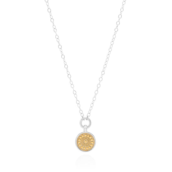 A delicate silver chain necklace featuring a small round pendant with a textured gold center and a clear crystal halo, displayed on a clean white background.