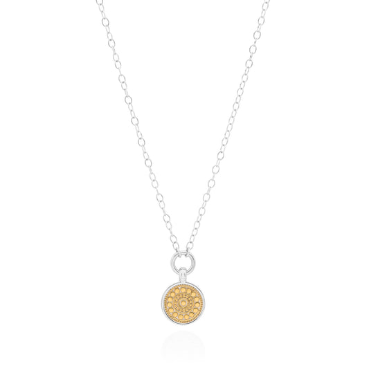 A delicate silver chain necklace featuring a small round pendant with a textured gold center and a clear crystal halo, displayed on a clean white background.