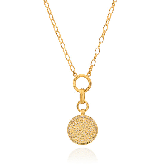 A gold chain necklace featuring a round, textured pavé-style disc pendant suspended from a ring clasp, shown on a clean white background with a subtle reflection.
