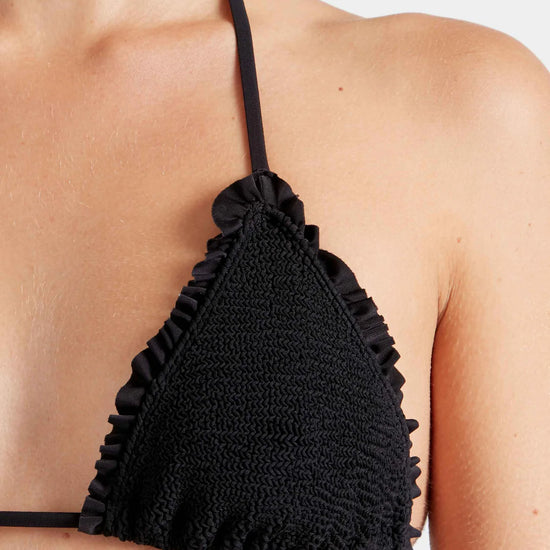 Woman wearing black triangle bikini top by Hunza G with ruffled details on a white background