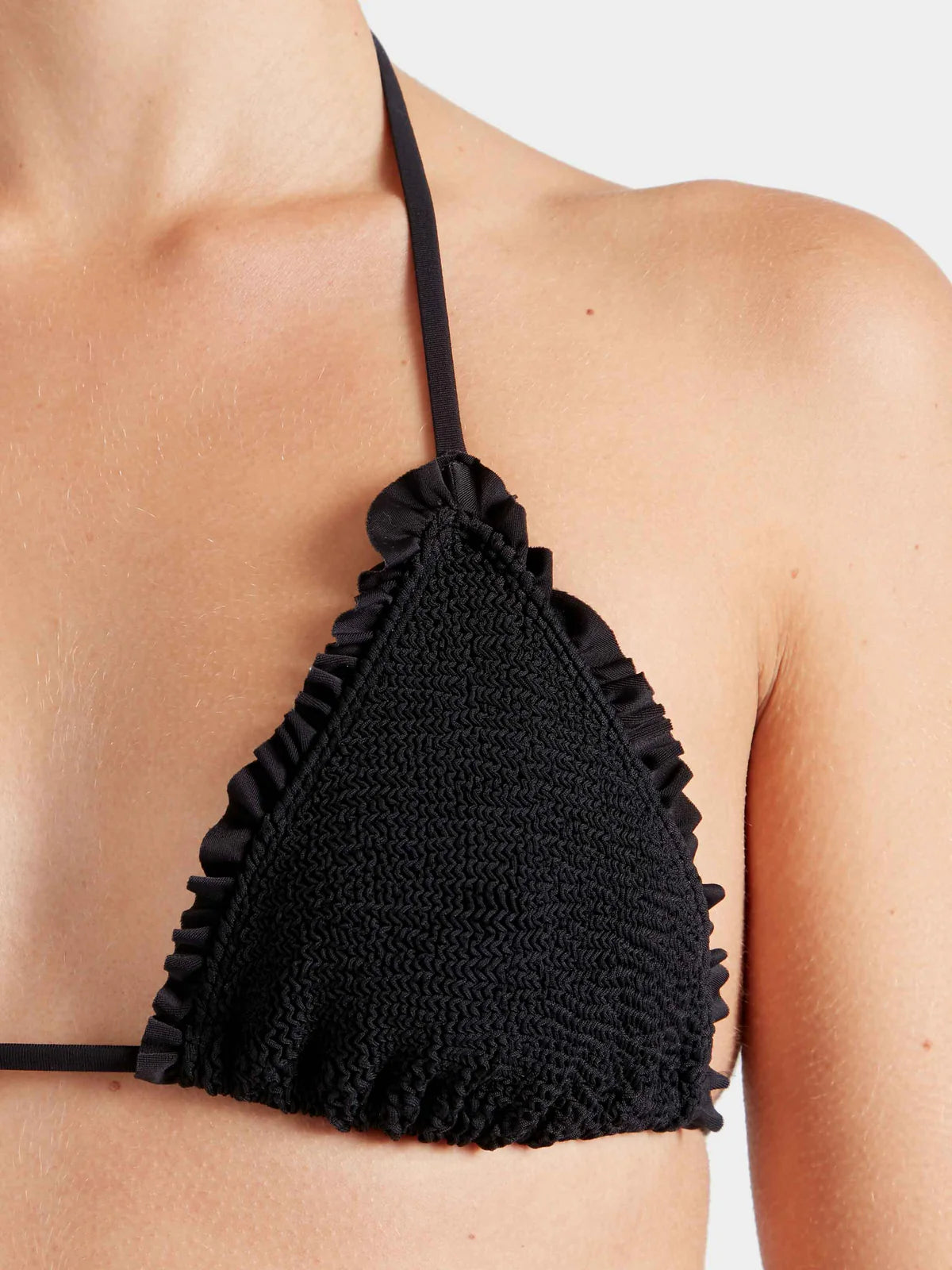 Woman wearing black triangle bikini top by Hunza G with ruffled details on a white background