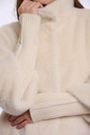 Close-up of a person wearing a cream-colored faux fur sweater with ribbed knit cuffs and collar, showing the soft texture and warm off-white color.