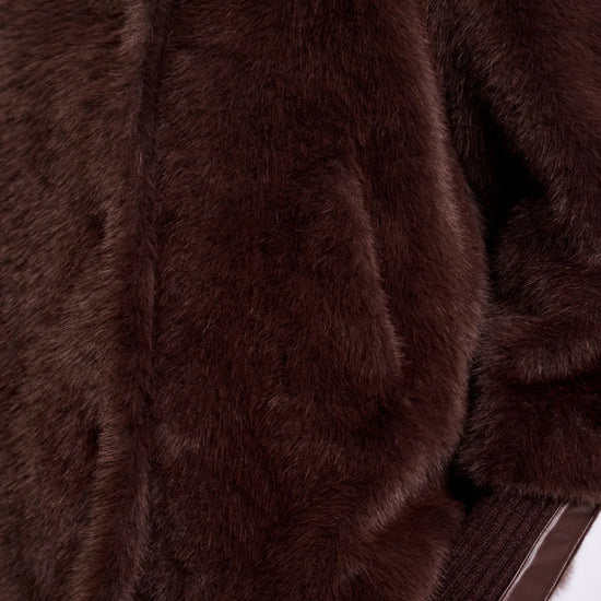 Close-up of a dark brown faux fur jacket with a ribbed brown knit sleeve, shown on a model wearing dark brown pants against a white background.