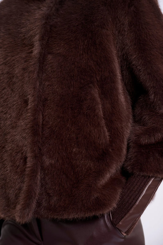 Close-up of a dark brown faux fur jacket with a ribbed brown knit sleeve, shown on a model wearing dark brown pants against a white background.