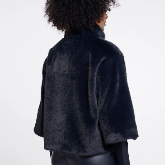 A model shown from the back wearing a dark navy blue fuzzy cropped jacket and black pants against a light gray studio background.