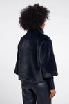 A model shown from the back wearing a dark navy blue fuzzy cropped jacket and black pants against a light gray studio background.
