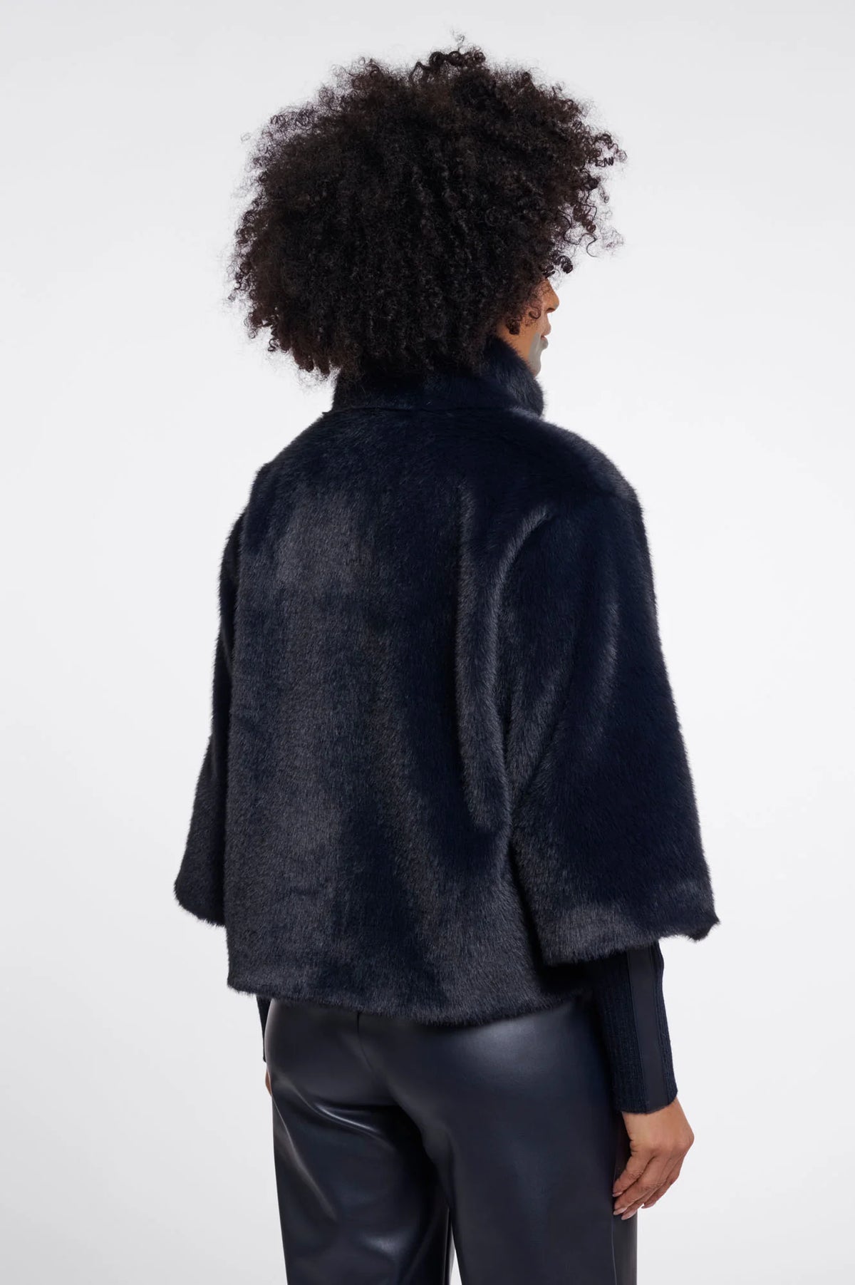 A model shown from the back wearing a dark navy blue fuzzy cropped jacket and black pants against a light gray studio background.