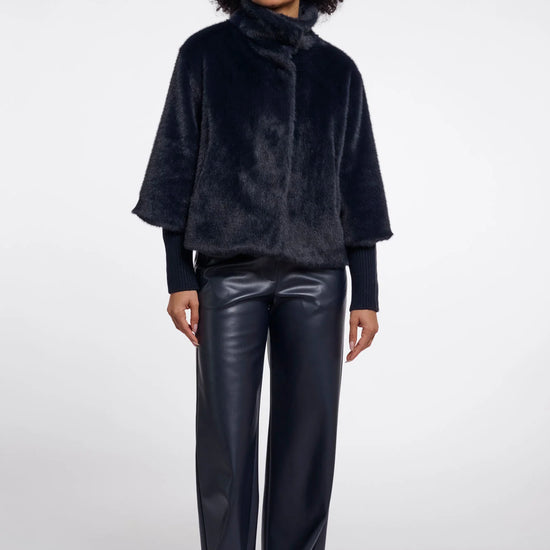 Woman wearing a dark blue textured jacket and black leather pants on a white background