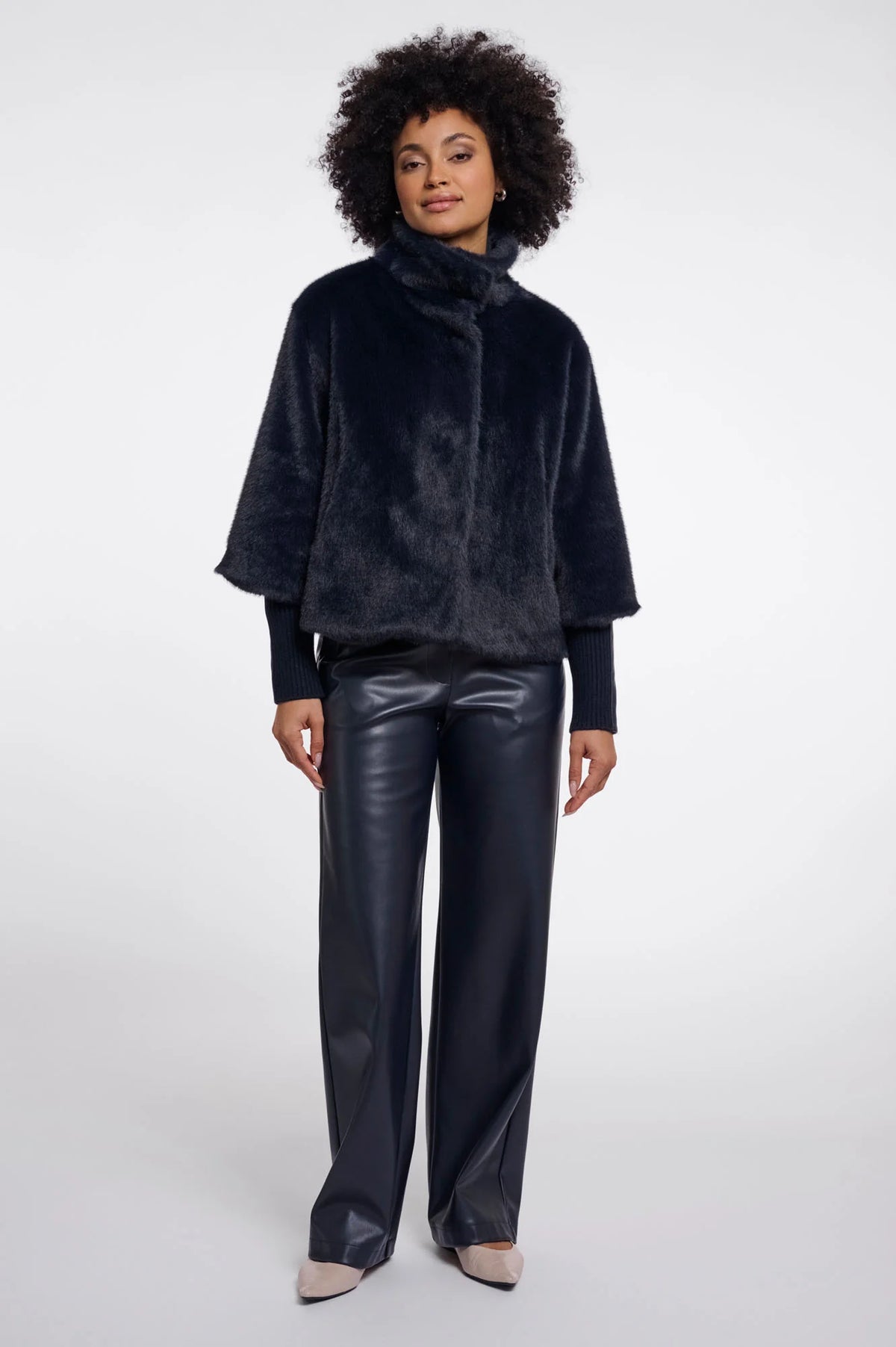 Woman wearing a dark blue textured jacket and black leather pants on a white background