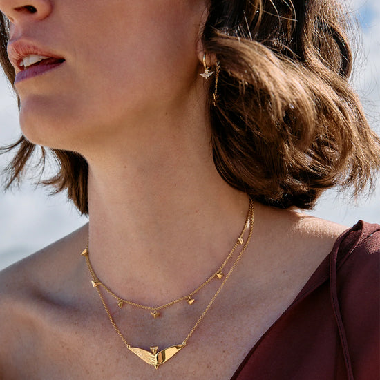 Woman wearing a gold necklace with a blurred natural background
