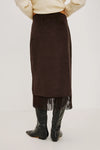 model wearing a brown skirt with fringe detail on the hem facing away from the camera 
