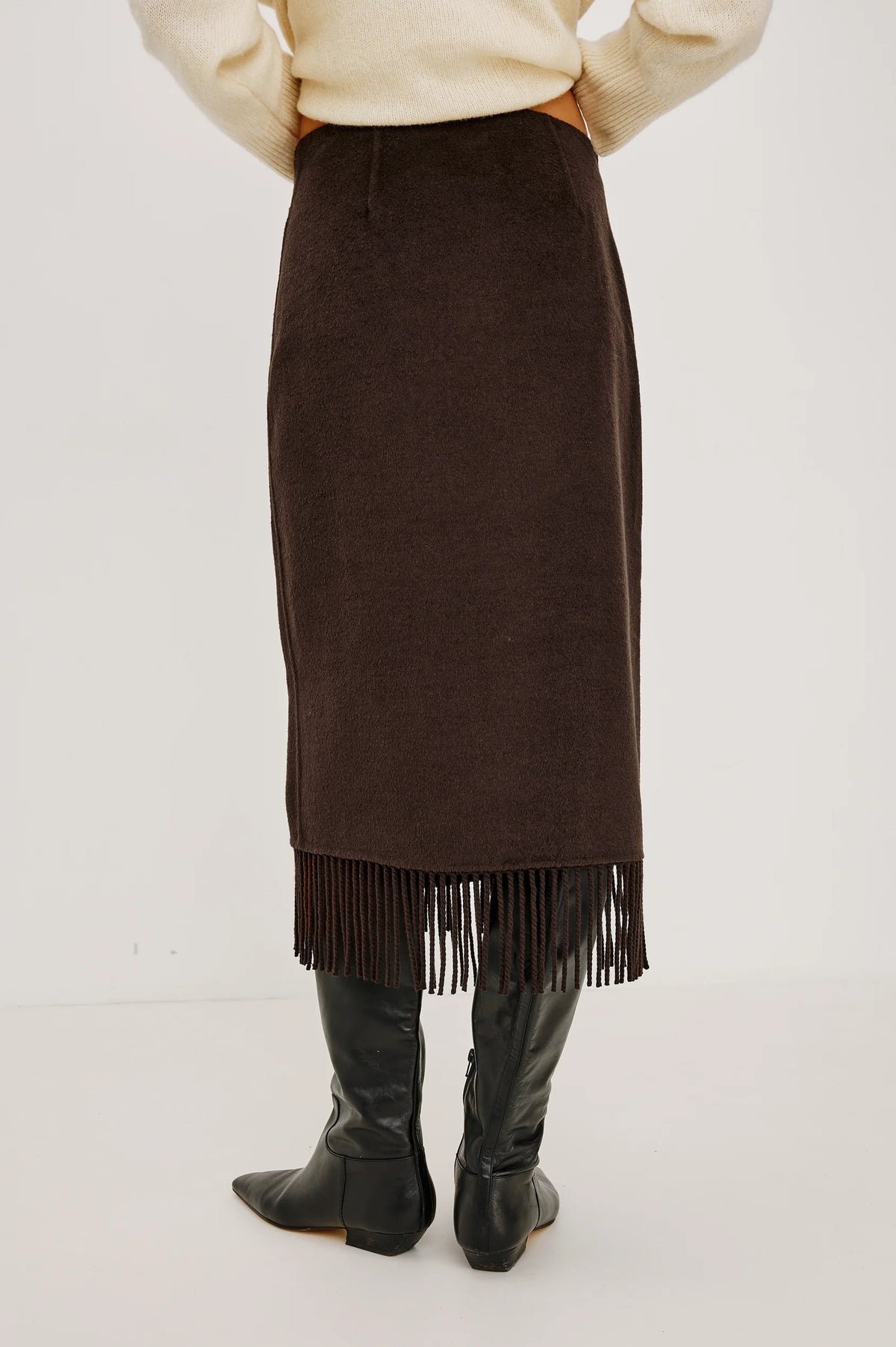 model wearing a brown skirt with fringe detail on the hem facing away from the camera 