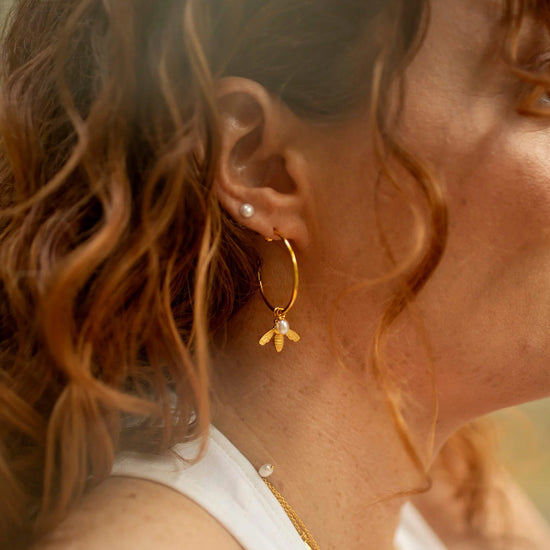 Large gold hoop earrings with flying bee pendants and a rice pearl drop with butterfly earring fastenings