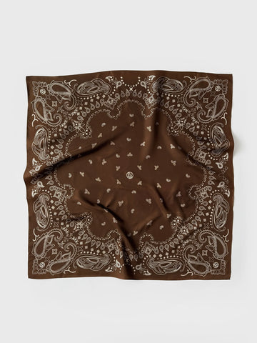 A square brown bandana featuring a classic paisley pattern in light beige, laid flat on a light gray background.