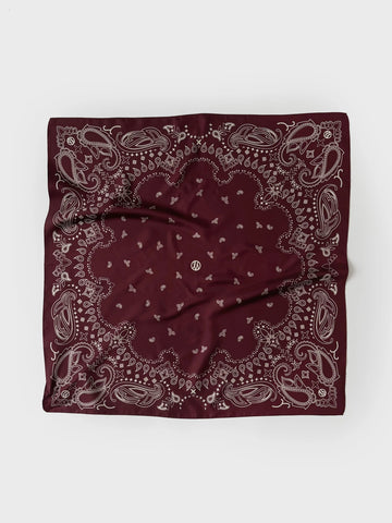 A square bandana in deep burgundy with a detailed paisley pattern in light gray, laid flat on a light gray background.