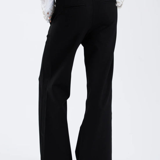 Black bell-bottom pants worn with a white shirt on a white background rear view