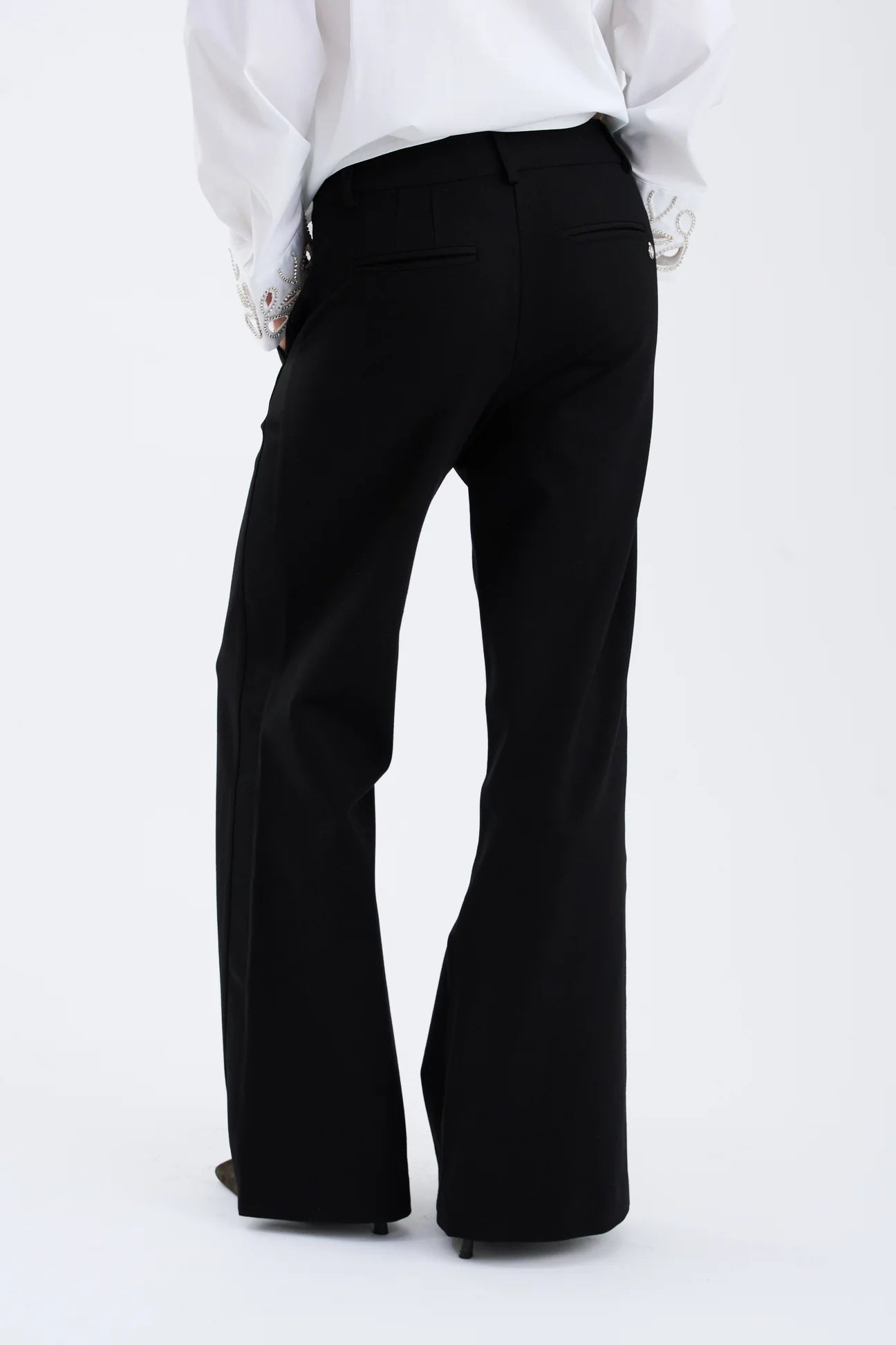 Black bell-bottom pants worn with a white shirt on a white background rear view