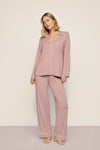 A woman modeling a two-piece dusty rose pajama set with white piping details, consisting of a long-sleeve button-up shirt and matching wide-leg pants, against a neutral studio backdrop.