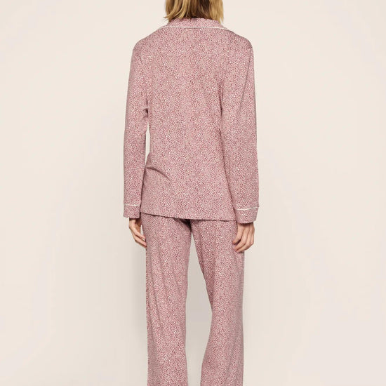 A woman viewed from behind wearing a matching two-piece pajama set with a textured, speckled pattern in dusty pink and white. The set includes a long-sleeve top and wide-leg pants, photographed against a neutral, light beige studio background.
