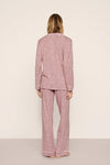 A woman viewed from behind wearing a matching two-piece pajama set with a textured, speckled pattern in dusty pink and white. The set includes a long-sleeve top and wide-leg pants, photographed against a neutral, light beige studio background.
