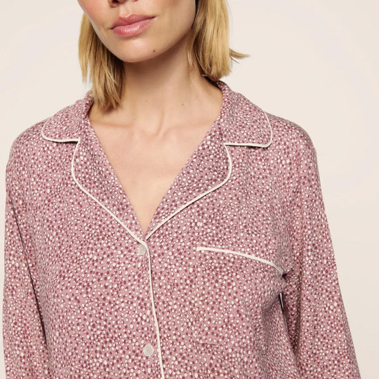 A close-up of a woman wearing a pink and white patterned long-sleeve pajama top with white piping details, set against a plain light beige background.