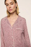 A close-up of a woman wearing a pink and white patterned long-sleeve pajama top with white piping details, set against a plain light beige background.