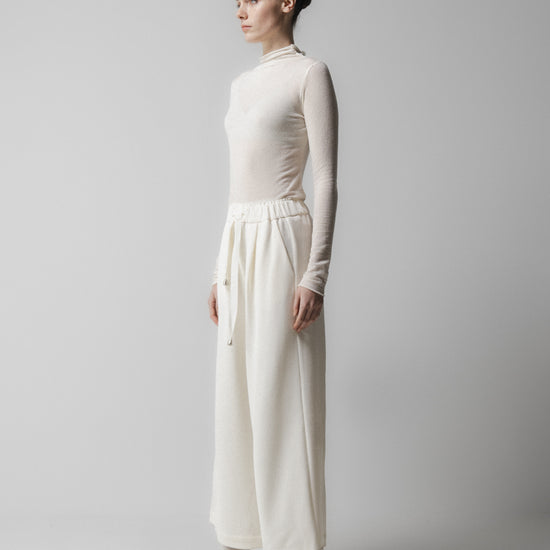 Person wearing a white outfit with a high collar and wide-leg pants on a plain background from Emin + paul