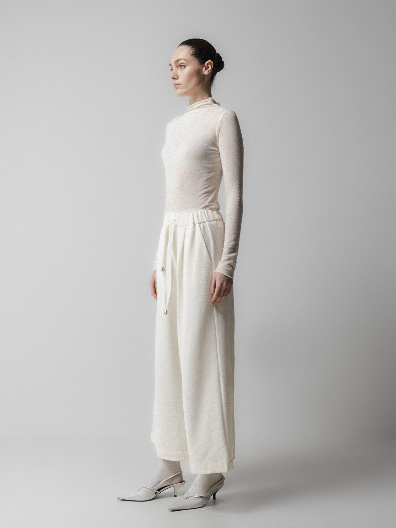 Person wearing a white outfit with a high collar and wide-leg pants on a plain background from Emin + paul