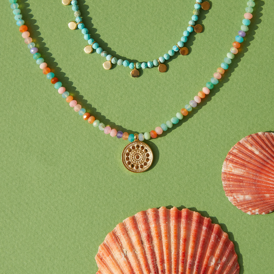 Two beaded Anna Beck necklaces on a green background with shells