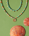 Two beaded Anna Beck necklaces on a green background with shells