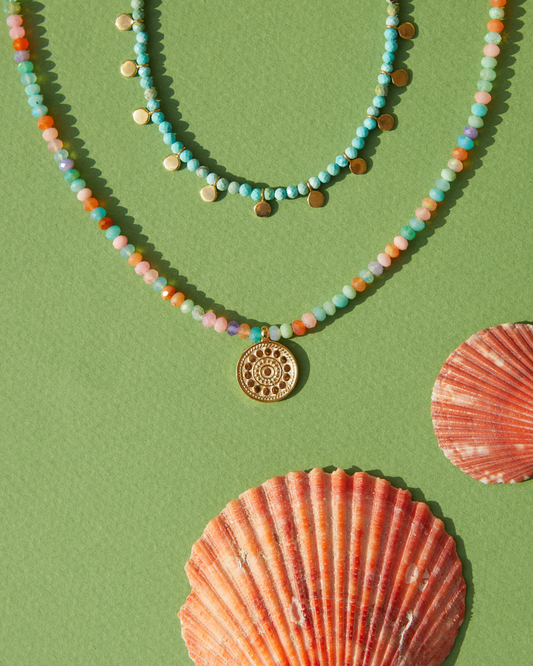 Two beaded Anna Beck necklaces on a green background with shells