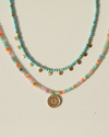 Two beaded necklaces with a gold pendant by Anna Beck on a light background