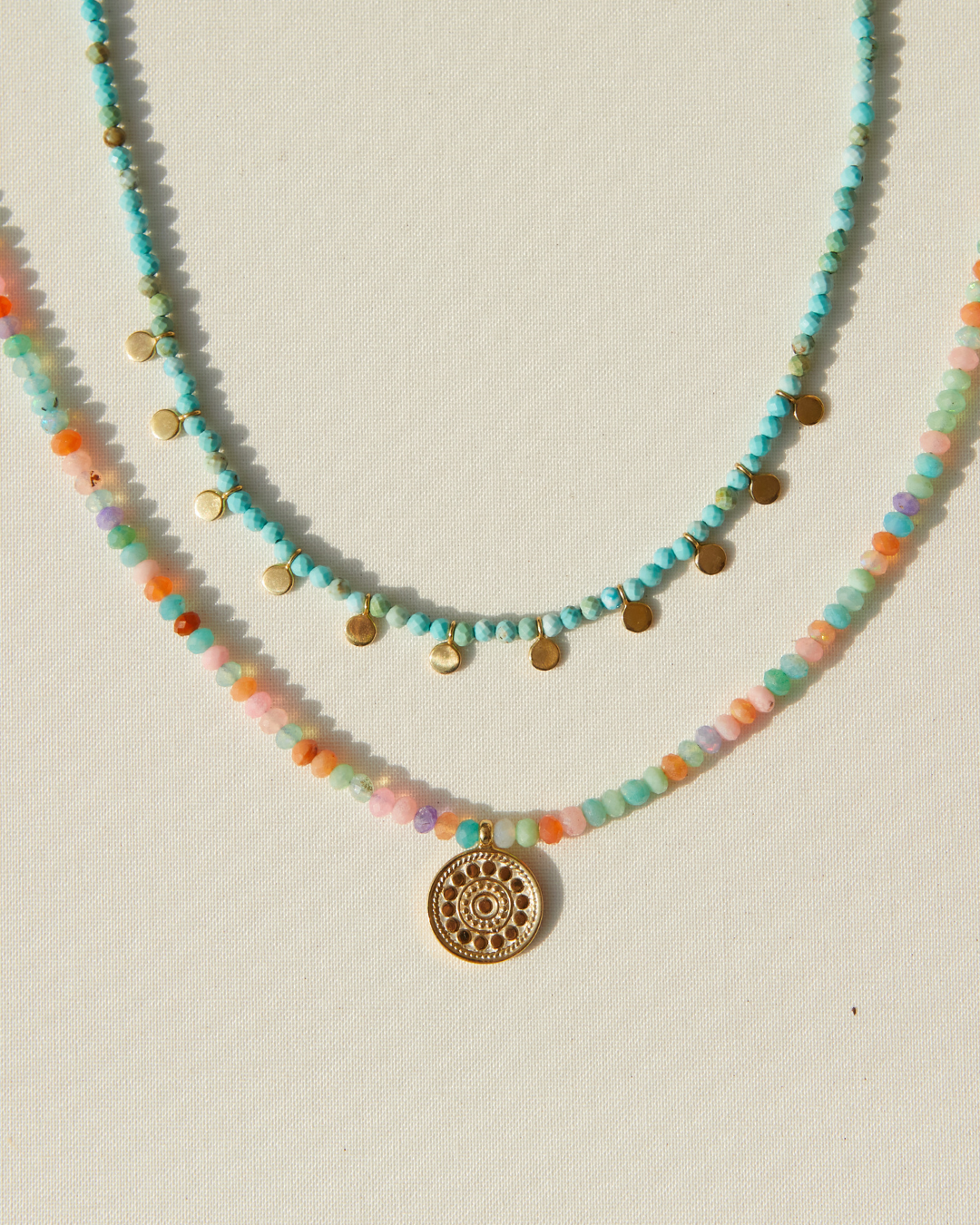 Two beaded necklaces with a gold pendant by Anna Beck on a light background