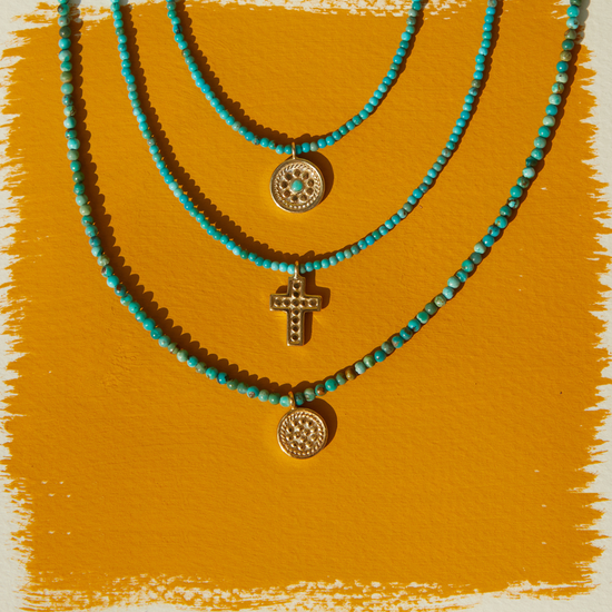 Three turquoise beaded necklaces with gold pendants on a mustard yellow background