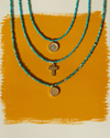 Three turquoise beaded necklaces with gold pendants on a mustard yellow background