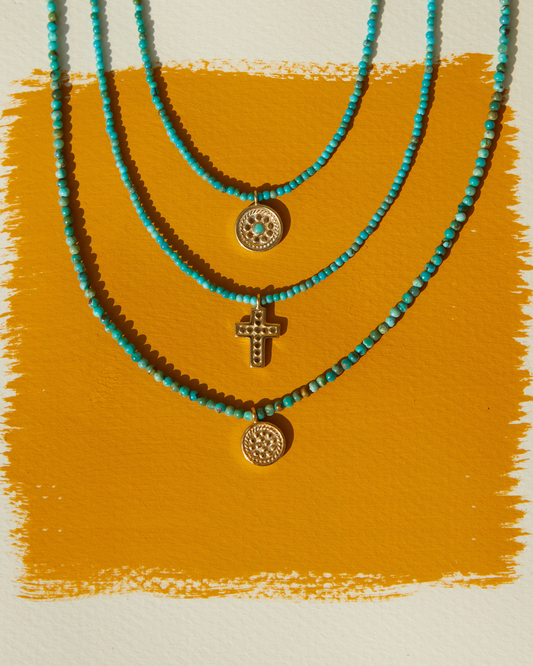 Three turquoise beaded necklaces with gold pendants on a mustard yellow background
