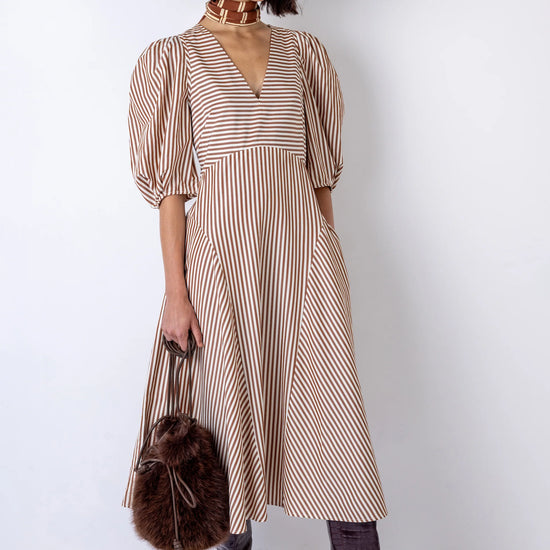 Woman wearing a striped dress holding a fur bag against a white background