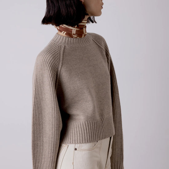 Person wearing a beige sweater and light-colored pants against a plain background