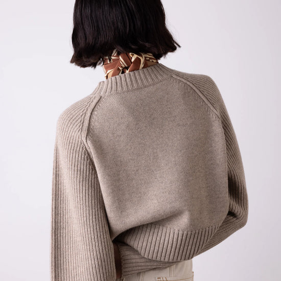 Person wearing a beige sweater and beige pants on a white background