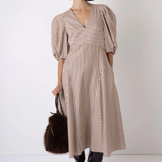 Woman wearing a striped dress with black boots and a brown bag on a white background