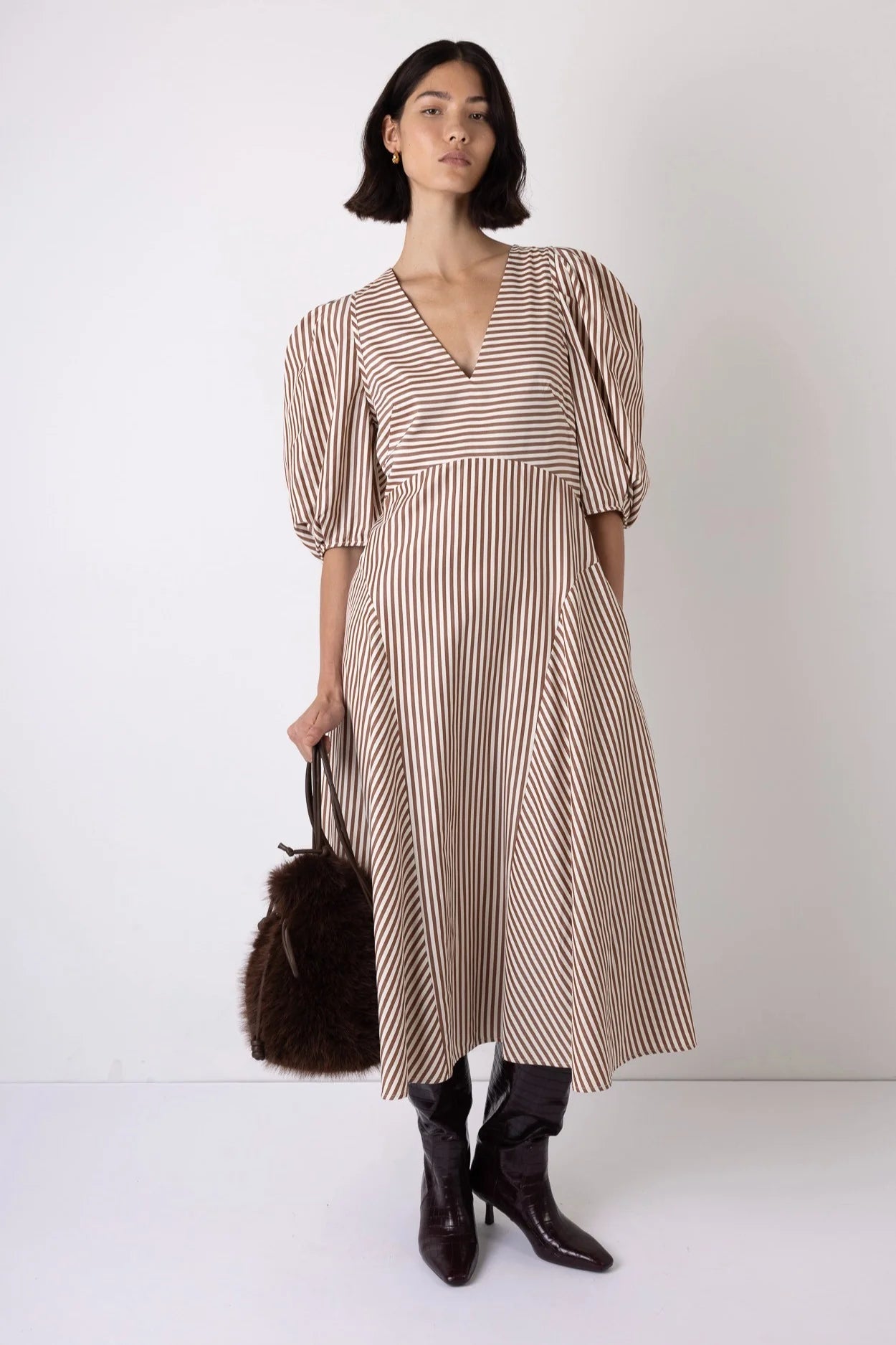 Woman wearing a striped dress with black boots and a brown bag on a white background