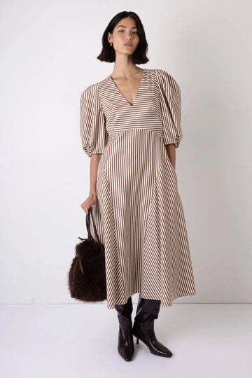 Woman wearing a striped dress with black boots and a brown bag on a white background