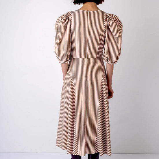 Person wearing a beige and brown striped dress against a white background