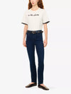 A model wearing a white short-sleeve t-shirt with black lettering on the chest and black ringer trim on the sleeves, paired with dark blue skinny jeans, a black belt, and dark brown leather flats, against a plain white background.