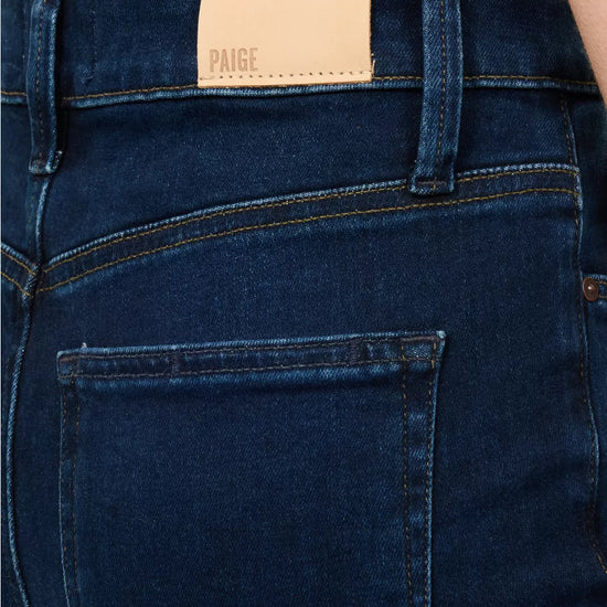 A model wearing a white short-sleeve t-shirt with black lettering on the chest and black ringer trim on the sleeves, paired with dark blue skinny jeans, a black belt, and dark brown leather flats, against a plain white background.