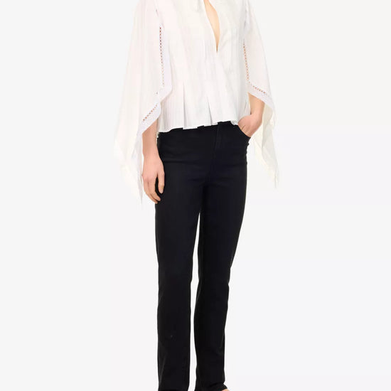A woman modeling a white sheer long-sleeve blouse with a tie neckline and black pants, standing against a plain white studio background.