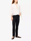 A woman modeling a white sheer long-sleeve blouse with a tie neckline and black pants, standing against a plain white studio background.
