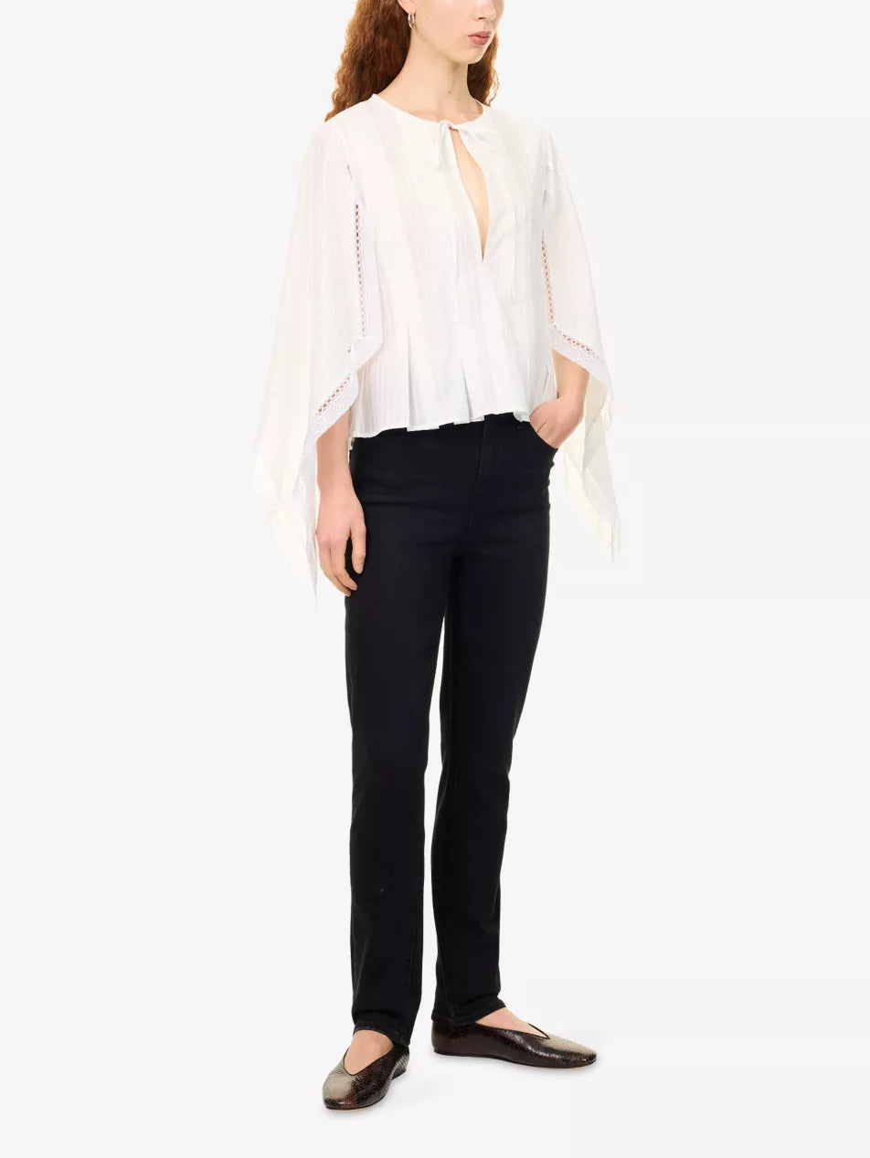 A woman modeling a white sheer long-sleeve blouse with a tie neckline and black pants, standing against a plain white studio background.