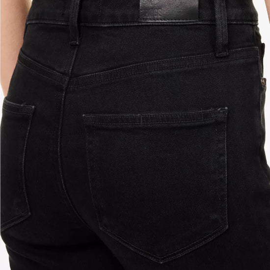 Close-up back view of a person wearing black denim jeans, showing the waistband, belt loops, and back pocket details.